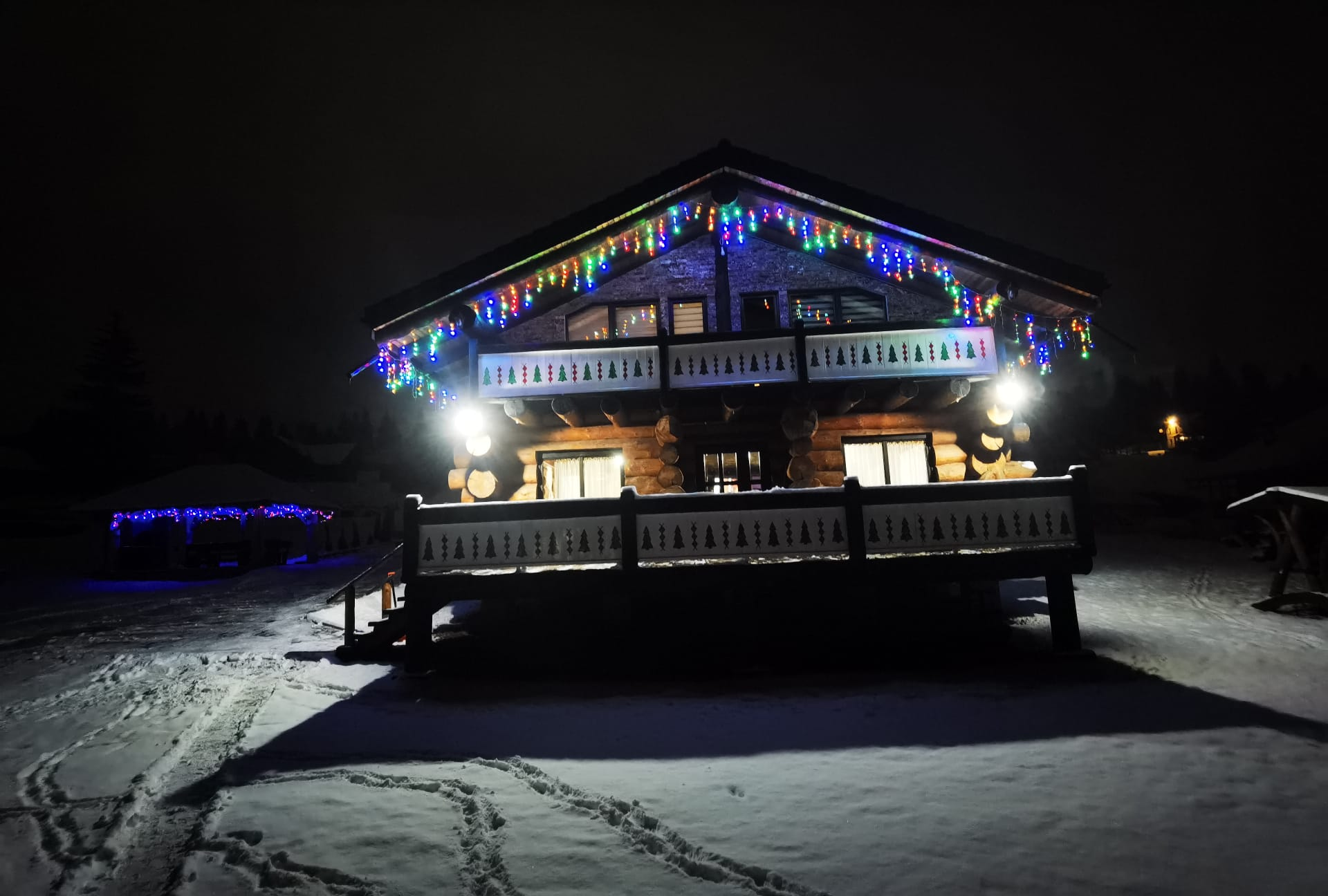 Cabana cu brăduți luminată într-o noapte de iarnă